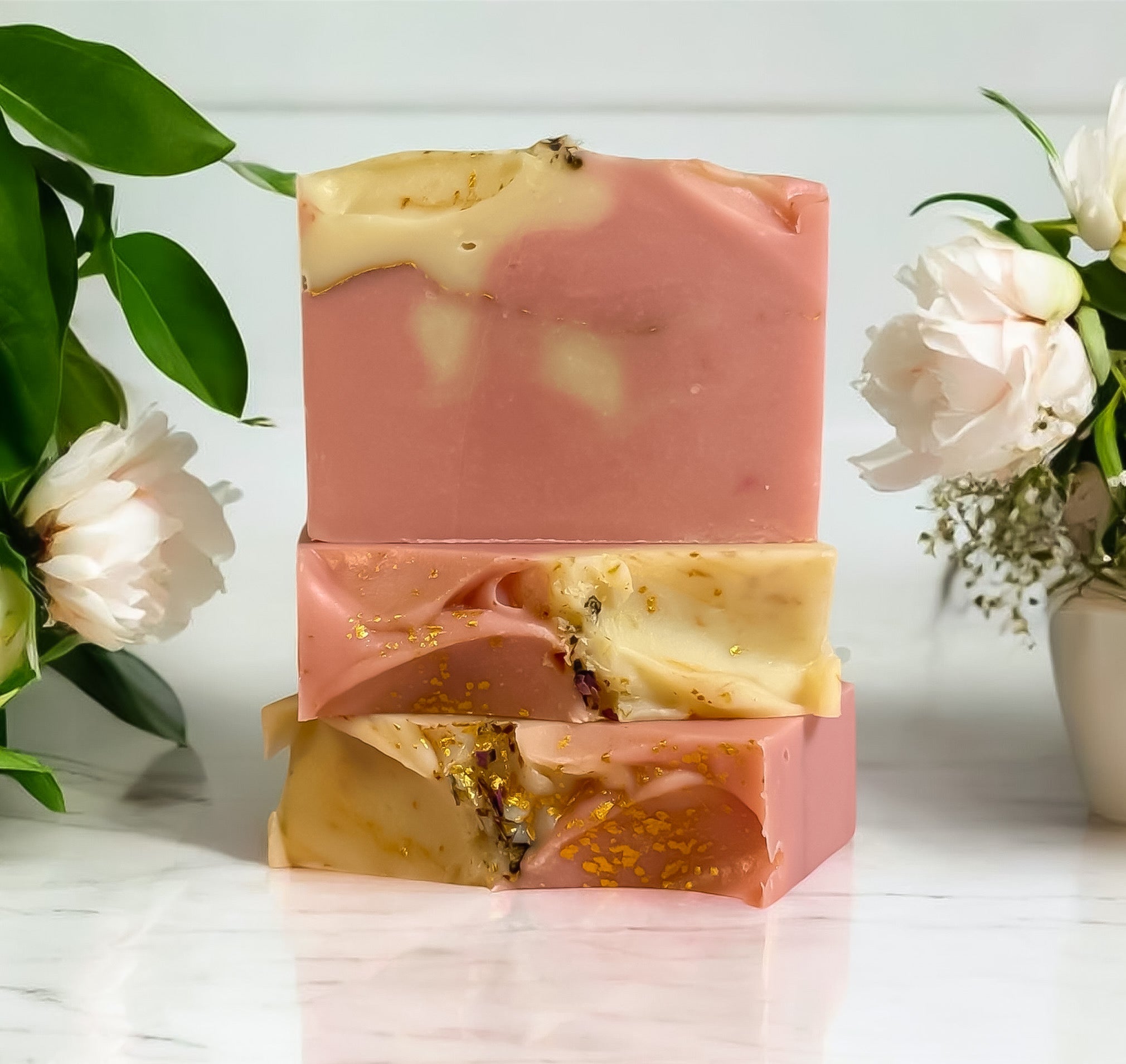Stack of pink and gold soap bars with flowers and greenery in the background