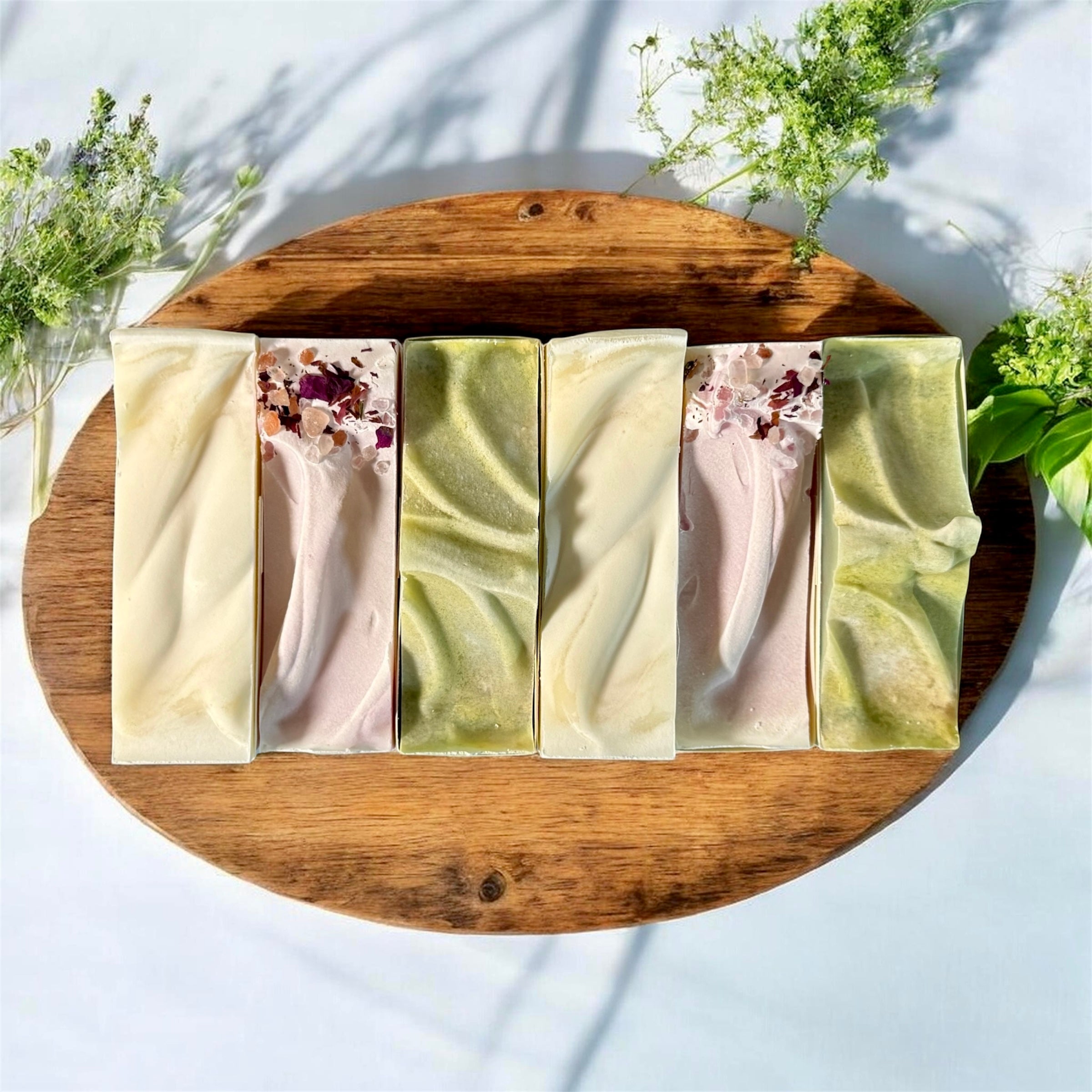 Six bars of handmade process soap in a stack sitting on a wooden cutting board